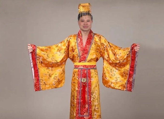 A man wearing an ornate golden and red traditional Chinese emperor costume with wide sleeves and an imperial headpiece.