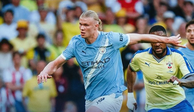 Action photo of footballer Erling Haaland in a Manchester City jersey competing against a player in a yellow Club América kit with "P&O CRUISES" sponsorship during a match.