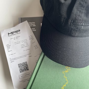 A black baseball cap resting on a green box next to a printed MPP receipt and a black booklet or card with text including 'mpp.com.vn' and a QR code.