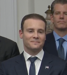 Two men in dark suits with American flag lapel pins stand in a formal indoor setting, with the man in the foreground smiling slightly while the bearded man behind him wears a blue striped tie. The formal, official atmosphere of the image contrasts humorously with the casual, enthusiastic caption referencing Hyperliquid, suggesting the formal-looking figures are being meme-ified as "knowing what's up" with the crypto trading platform.
