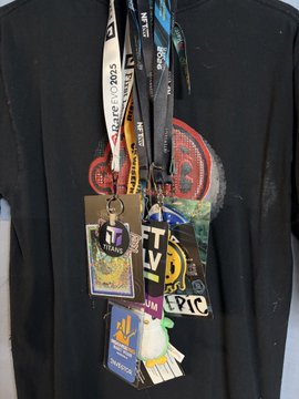 A person wearing a black t-shirt with multiple event lanyards and badges hanging from their neck, including ones with 'LIVE', '10', and 'EPIC' visible.