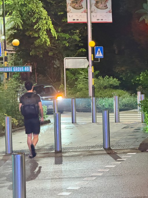 A man with a backpack walks past metal bollards on Orange Grove Road, his back to the camera, humorously framed as "Jeff" with invisible bodyguards ready to ambush unsuspecting photographers.