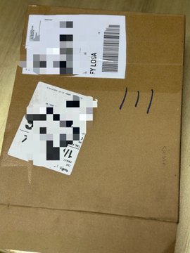 A cardboard shipping box with a partially blurred shipping label showing 'SYLOCA' and handwritten '111' on top.