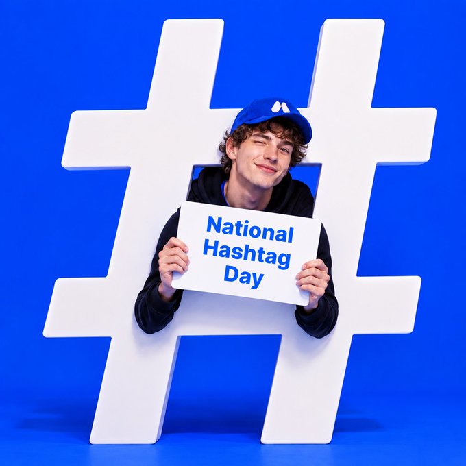 A promotional graphic for National Hashtag Day features a smiling young man wearing a blue cap holding a sign that reads 'National Hashtag Day' in front of a large white hashtag symbol on a blue background.