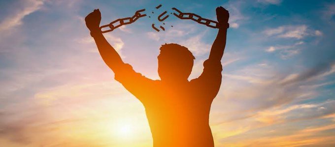 A silhouette of a person raises their arms triumphantly, breaking chains against a bright sunset sky.