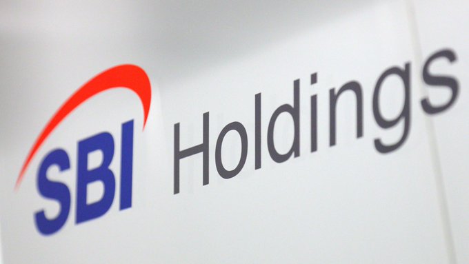 A close-up of the SBI Holdings logo is shown, featuring the company's name in dark blue lettering with a distinctive red swoosh above it, all displayed on a white background. The image represents the financial giant partnering with the Solana Foundation to launch SBI Solana Global, a joint venture focused on building onchain financial markets and issuing yen-backed stablecoins in Japan.