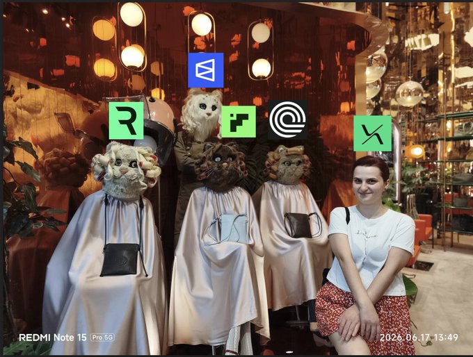 The image features a woman sitting next to a group of statues, each wearing a cape or a robe with a cat head design. There are five cats depicted in the scene, including one that has a "R" on its head. The woman is positioned behind these cat-themed statues and appears to be posing for the photo. The image also contains text related to Perp DEXs and strategies, which may suggest that this unique display of cat-themed statues could be associated with a Perp DEX or a similar event in the crypto world.