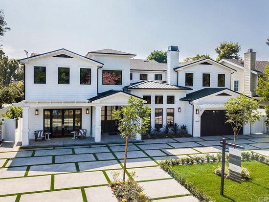 A large white modern-style two-story luxury house with black-framed windows, a manicured front yard with geometric stone pathways, and a dark front door, with a 'SOLD' sign visible.