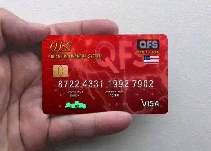 A hand holds a red 'QFS QUANTUM FINANCIAL SYSTEM DEBIT CARD' with a Visa logo, an American flag, and the card number 8722 4331 1992 7982.