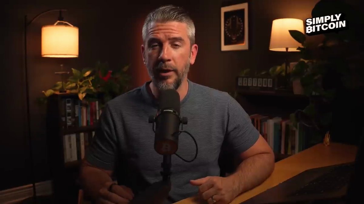 The image features a man sitting at a desk with a microphone, likely recording a podcast or live stream. The background of the image shows a bookshelf filled with various books, suggesting that he might be discussing topics related to finance, technology, or other subjects relevant to Bitcoin and cryptocurrency.