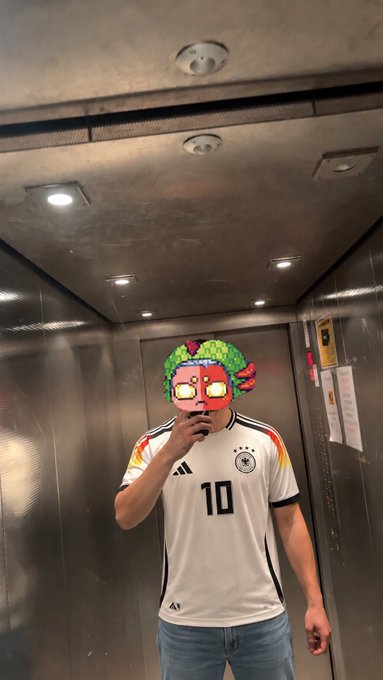 The image features a man wearing a soccer jersey with the number 10, standing inside an elevator. He is taking a selfie using his cell phone while wearing the soccer jersey. The caption of the photo reads "alright another day of selfie posting it’s world cup today $BASE is close good vibes are here Mexico easy win tonight polymarket bet is set wassup fam". This post seems to be related to the World Cup, as indicated by the caption and the soccer jersey worn by the man.