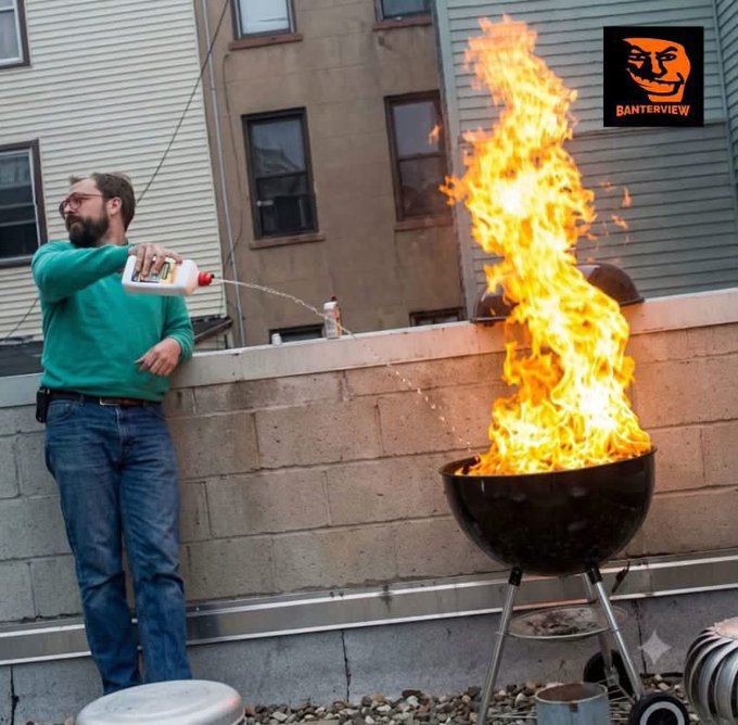A man in a green sweater and jeans pours liquid from a white bottle onto a flaming charcoal grill, with a 'BANTERVIEW' logo featuring a face in the top right corner.