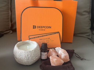 A promotional image showing a DEEPCOIN orange gift bag with a white ceramic candle holder, small bottle, pink Himalayan salt stones in a pouch, and a welcome card.