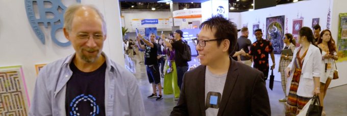 Two men stand together at what appears to be a convention or conference, with one wearing a Bitcoin-themed shirt and the other dressed in a blazer, both smiling. The accompanying post references a debate about UASF (User Activated Soft Fork) in the Bitcoin community, suggesting the image may be from a crypto-related event like a Bitcoin conference.