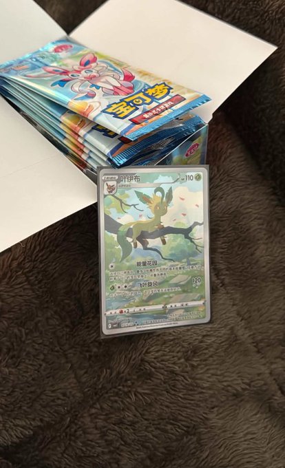 A stack of Chinese Pokémon Trading Card Game booster packs (Leafeon-themed) next to a Leafeon holographic card displayed on a brown textured surface.