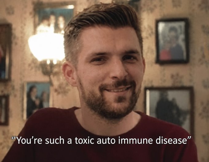 A man with short brown hair and a beard smiles in a room with patterned wallpaper and framed photos, with the caption 'You're such a toxic auto immune disease'.