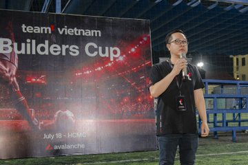 A man in a black shirt and glasses speaks into a microphone at a 'team vietnam Builders Cup' event (July 18, Ho Chi Minh City, by Avalanche).