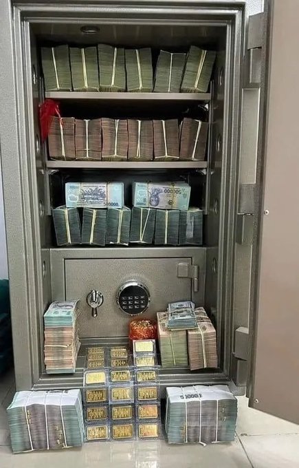 An open gray safe is filled with stacks of banded currency, bundles of cash in various denominations, and several gold bars arranged on the floor.