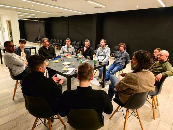 A group of about twelve people sit around a conference table in a modern meeting room, appearing to be in a discussion or workshop.