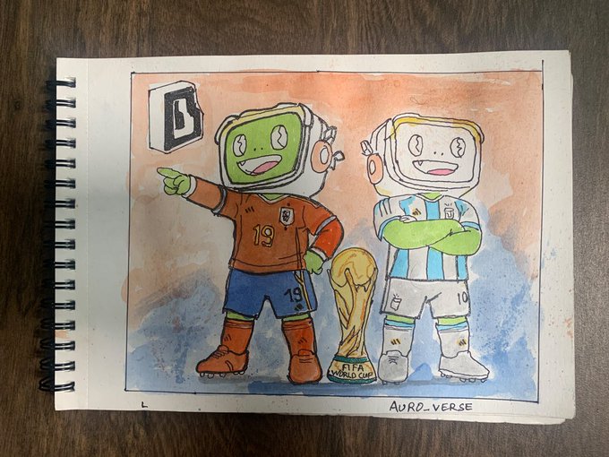 A watercolor painting in a spiral notebook depicting two cartoon characters in soccer uniforms (orange #19 and light blue/white #10) next to a FIFA World Cup trophy, signed 'AURDVERSE'.