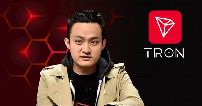 A man in a beige jacket over a black hoodie speaks in front of a red honeycomb background, with the TRON cryptocurrency logo displayed prominently on the right.