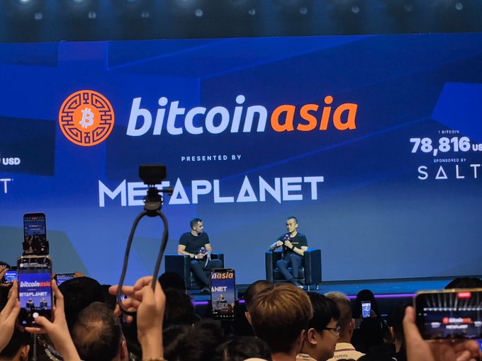 Two men sit on stage at the 'Bitcoin Asia' conference presented by Metaplanet, with a large screen behind them showing the BTC price sponsored by SALT.