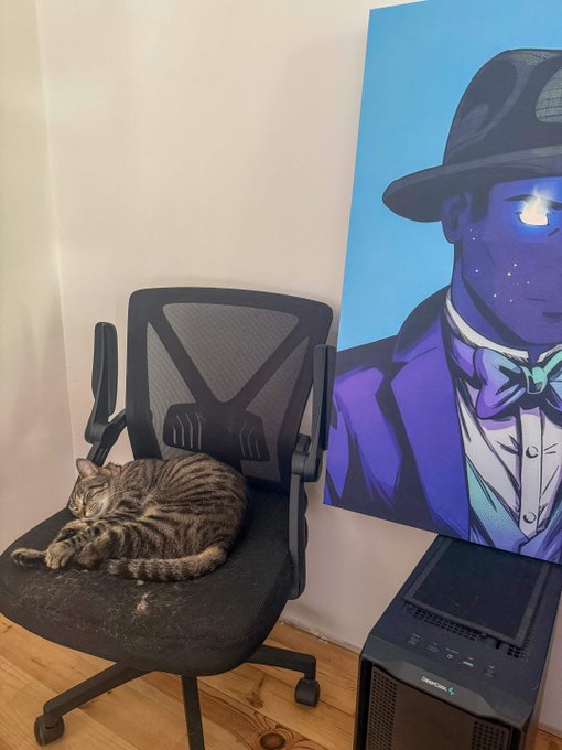 A tabby cat curled up sleeping on a black mesh office chair next to a painting of a dapper figure in a suit and bow tie with glowing eyes, with a computer tower visible below.