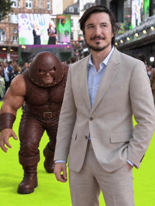 A man in a beige suit poses on a green carpet next to a person dressed in a Juggernaut costume, with crowds and venue structures visible in the background, visually accompanying the caption "The hottest chain in the crypto space" alongside @vladtenev and the word "Juggernaut!"