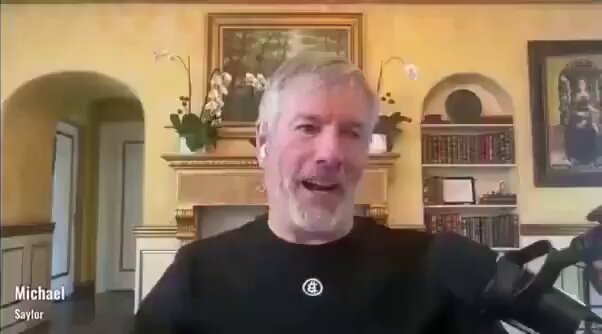 In this image, a man named Michael sits in front of a fireplace in a room. He appears to be wearing a black shirt as he speaks into a microphone during an interview or discussion. The background features a bookshelf filled with numerous books, adding depth and interest to the space. The image also includes several text elements, such as "Michael Said," "He's a good man," and "7.5% of the network". There is also some information about Michael's financial situation at the bottom, stating that he would receive $10,000,000 if he gets 7.5% of the network and then slow down his growth.