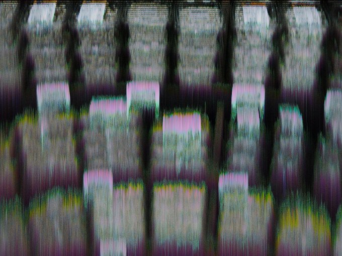 Abstract digital glitch art or distorted image with vertical streaks of pink, green, yellow, and dark colors creating a pixelated, static-like effect.