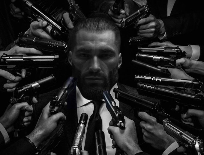 A bearded man in a suit stands stoically, surrounded by numerous hands pointing pistols at him from all sides in this black-and-white image, evoking a sense of being besieged. The post suggests that facing multiple market downturns is akin to enduring an overwhelming barrage of threats, emphasizing veteran resilience against the chaos of a bear market.