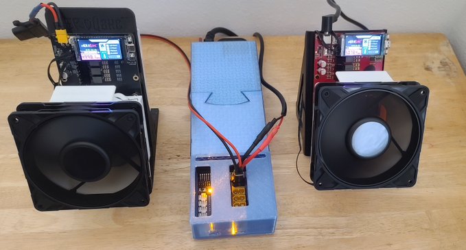 Two computer cooling fans connected to a labeled 'ToolkitRC' charger and a power supply with an ESP32 module displaying a screen, set up on a wooden surface.