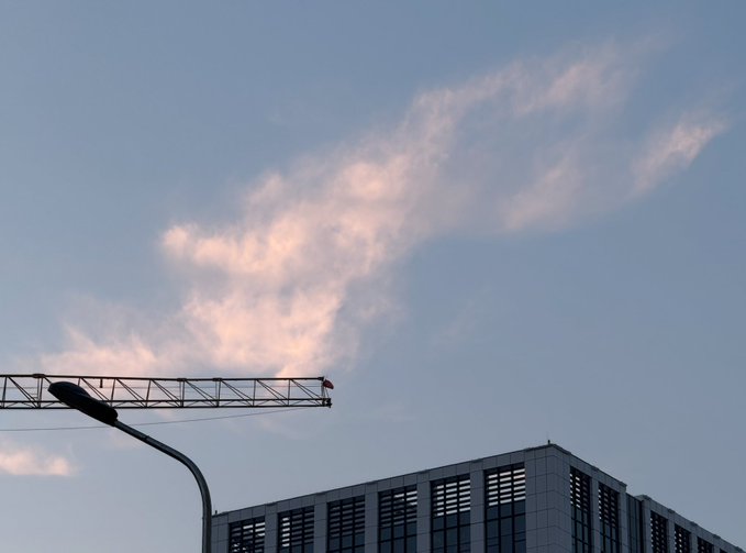 A serene dusk photograph of a construction crane silhouetted against a blue sky with pink-tinged clouds, above a modern building.