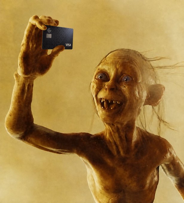 A creature resembling Gollum from Lord of the Rings holds up a small black Visa credit card against a tan background, smiling with its teeth showing.