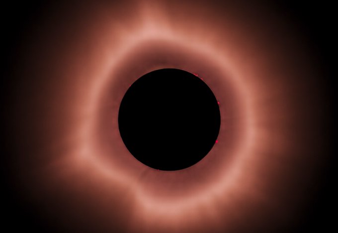 A total solar eclipse captured during the moment of totality, with the Moon's dark disk encircled by the Sun's glowing reddish-orange corona. The image serves as the foundation for the "Beyond the Shadow" NFT collection, which transforms this singular astronomical event into fine-art photography exploring the interplay of light and shadow.