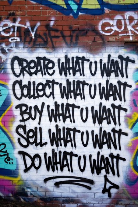 A graffiti mural on a white brick wall reads: 'CREATE WHAT U WANT, COLLECT WHAT U WANT, BUY WHAT U WANT, SELL WHAT U WANT, DO WHAT U WANT.'