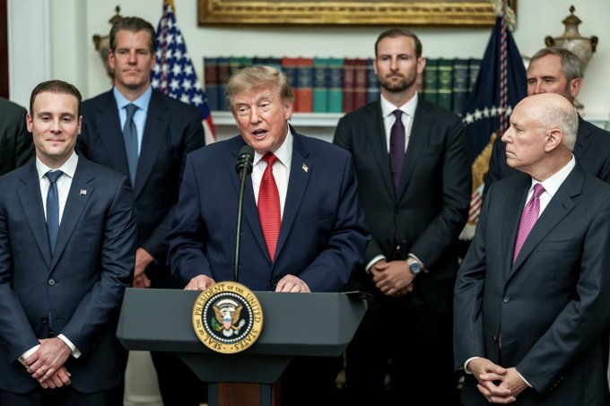 Donald Trump stands at a podium with the Seal of the President of the United States visible, flanked by several men in suits, likely representing a significant announcement that the accompanying post suggests impacted the crypto market.