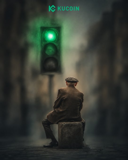 A lone man in a brown coat and flat cap sits on a concrete block, gazing at an illuminated green traffic light in a hazy urban street, with the "KuCoin" logo at the top—visually echoing the post's metaphor of waiting for the "green light" breakout.
