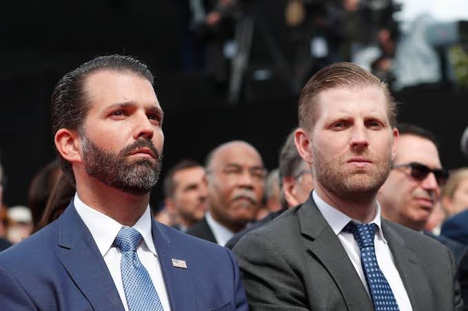 Donald Trump Jr. and Eric Trump attend a public event in suits, representing the Trump family's growing presence in cryptocurrency through ventures like $WLFI, USD1, and American Bitcoin.