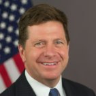 A headshot of Jay Clayton, former SEC Chair, smiling in front of an American flag backdrop. The image accompanies a breaking news announcement that he has been appointed by Trump to lead a new AI task force.