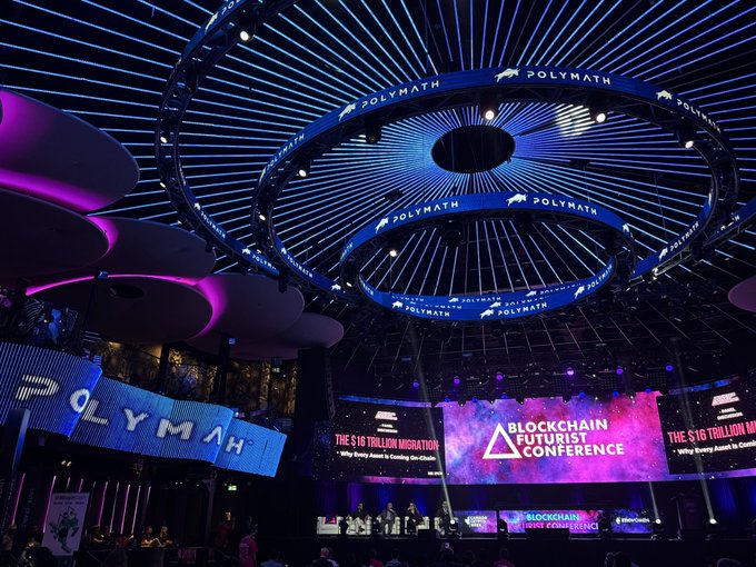 An elaborate conference stage setup with circular LED ceiling displays branded "POLYMATH" and a main screen reading "BLOCKCHAIN FUTURIST CONFERENCE" with side banners about "THE $16 TRILLION MIGRATION."