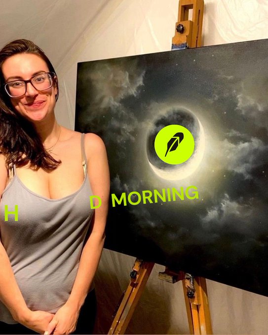 A pregnant woman with glasses wearing a gray tank top stands smiling next to a painting of a solar eclipse on an easel, with the text 'GOOD MORNING' overlaid on the image.
