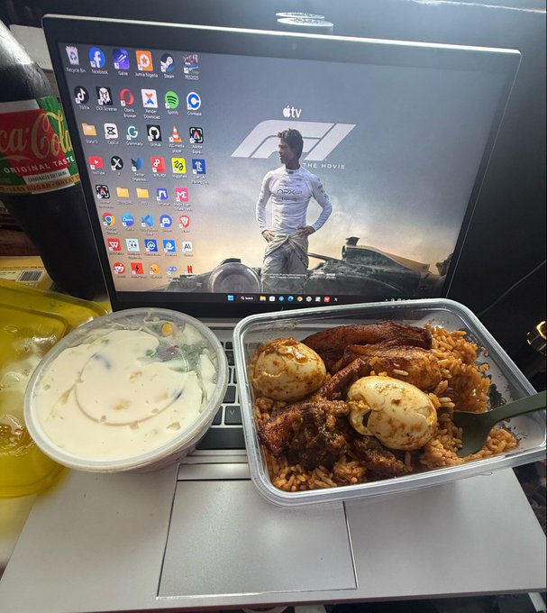 A tray of chicken and rice with a side salad sits on an airline seat tray table in front of a monitor displaying the "F1 THE MOVIE" desktop wallpaper, alongside a Coca-Cola bottle. The post humorously pairs this in-flight meal with a $ANSEM crypto discussion, suggesting the trader is "fueled up" for a bullish afternoon.