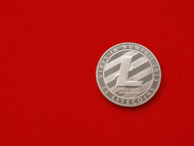 A silver Litecoin coin inscribed with "VIRES IN NUMERIS," "2.5," "TROY OUNCE .999 FINE SILVER," and "LITECOINS 2013" rests on a red surface, symbolizing the cryptocurrency referenced in the Litecoin Core v0.21.5.6 update announcement.