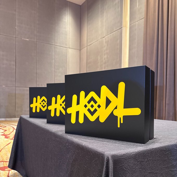 Three black display boxes with bold yellow "HODL" lettering sit on a gray-covered table, visually reinforcing the rallying cry "If you can't HODL, ___" by showcasing the iconic crypto slang term as a centerpiece of the message.