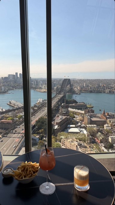 Drinks and fries on a high table overlooking Sydney Harbour, with the Sydney Harbour Bridge and city skyline visible through the window.