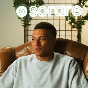 The image features a man sitting comfortably in a brown leather chair, wearing a gray sweatshirt with white text. The background of the photo shows a green plant behind him, which adds a touch of nature to the scene. The main focus of the image is on the man and his relaxed posture while seated in the chair.
