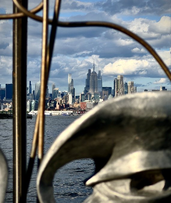 A view of the New York City skyline from across the water, framed by a metal sculpture in the foreground.