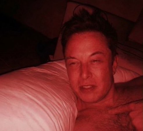 A man lying in bed with a pillow, illuminated by red lighting, appearing to be in a relaxed or sleepy state.