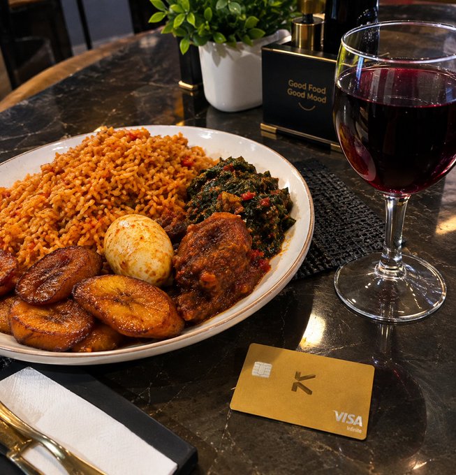 A plated meal of jollof rice, plantains, stewed greens, egg, and chicken sits on a dark table beside a glass of red wine and a gold Visa Infinite card marked with "K".